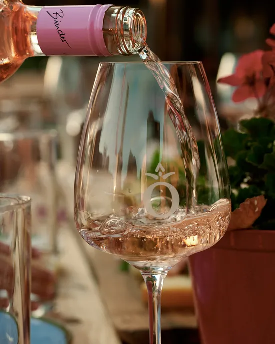 Roséwein wird in ein Glas auf einem gedeckten Außentisch mit Brot und Blumen eingeschenkt